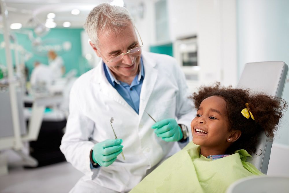 Happy girl on dental chair after repairing tooth with dentist sitting next to her children's oral health general dentistry dentist in Allen Texas